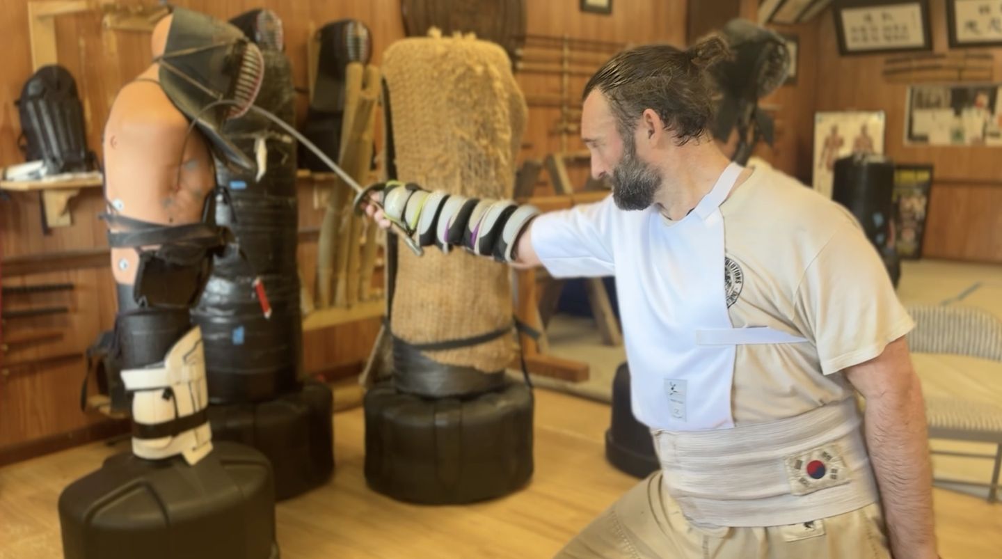A martial artist thrusts a training sword into a striking dummy in the dojang