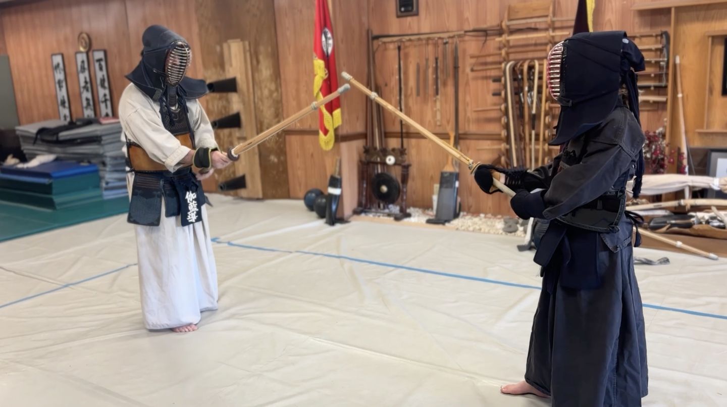 Two practitioners in kendo armor crossing bamboo swords in the training hall